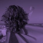 view of the back of a child wearing a cape, on a beach. Purple filter.