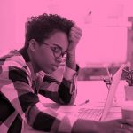 person at desk with head in hand looking exhausted, pink filter.