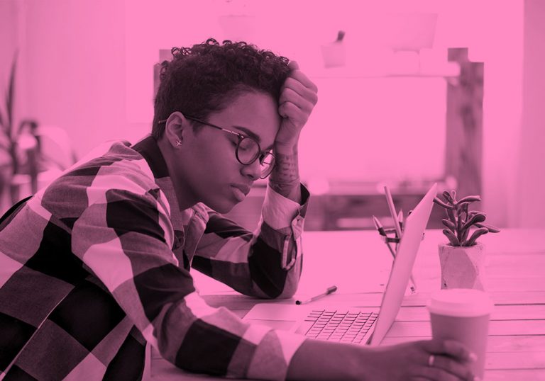 person at desk with head in hand looking exhausted, pink filter.