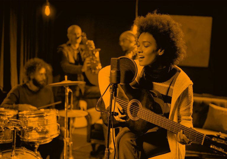 woman playing guitar and singing with band; orange filter